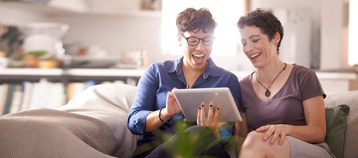 Zwei Frauen schauen lachend auf ein Tablet und laden Formulare herunter