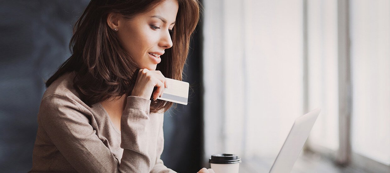 Frau mit Bankkarte in der Hand sitzt vor ihrem Laptop