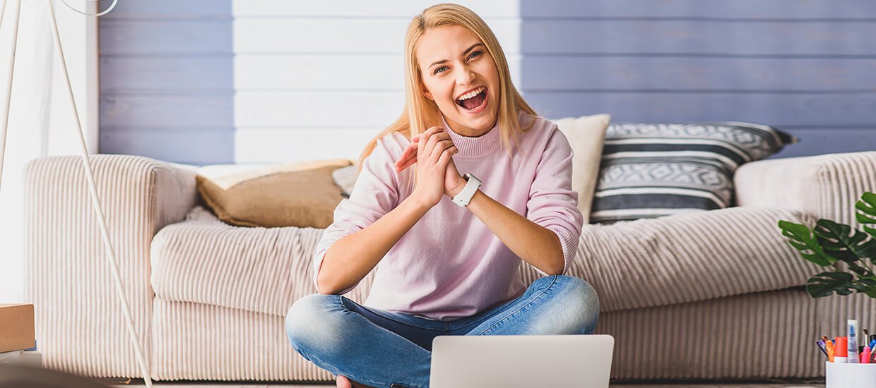 Lachende Frau sitzt im Wohnzimmer vor Ihrem Laptop