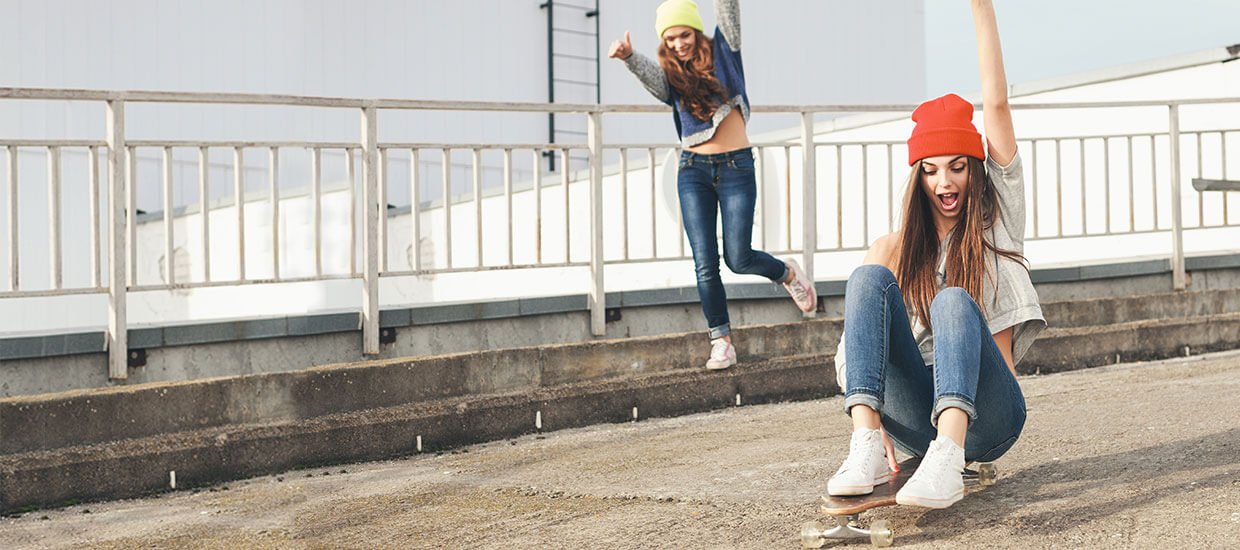 Zwei Mädchen haben Spaß und fahren sitzend auf einem Skateboard