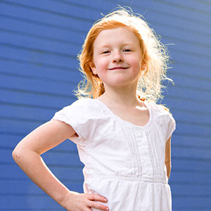 Rothaariges Mädchen steht selbstbewusst lächelnd vor einer blauen Wand