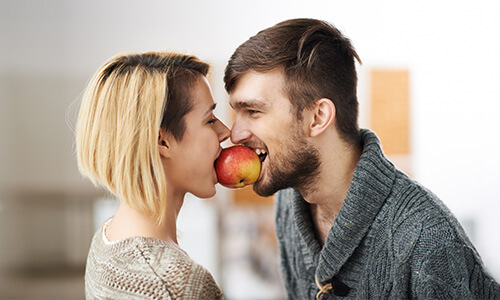 Paar balanciert zwischen den Gesichtern einen Apfel